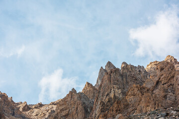 Scenic alpine landscape with sunlit rocky mountains in cloudy sky. Colorful mountain scenery with sharp rocks in sunlight under cirrus clouds. Awesome view to high rockies in sunshine in cloudiness.