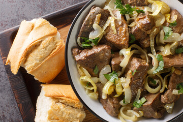 Grilled Liver with Onions closeup in the bowl served with bread on the table. Horizontal top view from above