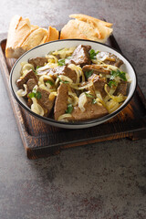 Close-up fried beef liver with onions served in a plate on a wooden tray. vertical