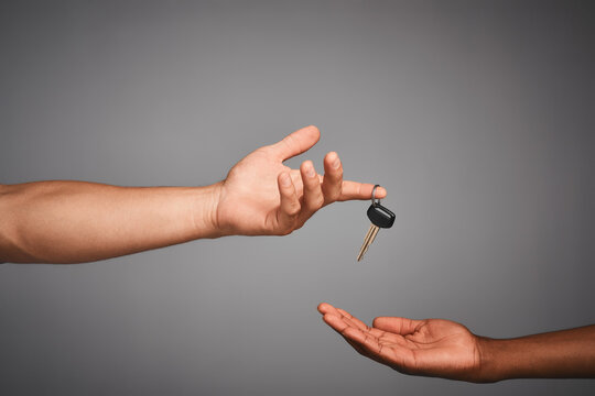 Handing Over Keys To The Designated Driver. Studio Shot Of Unidentifiable Hands Exchanging Keys Against A Gray Background.