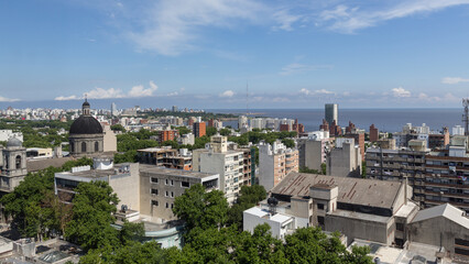Stadtbild Montevideos, mit weißen Gebäuden sowie Hochhäusern vor der sonnigen Küste und des blauen Wassers des Pazifiks.