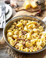 Pasta Pipe Rigate with stew In Bianco in a frying pan on a gray wooden culinary background. Traditional Italian pasta with ground beef on the kitchen table