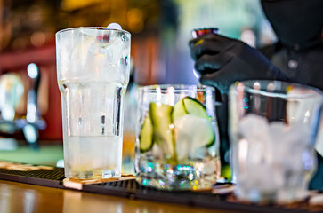 hands of a bartender with black gloves making cocktail on a bar counter.
