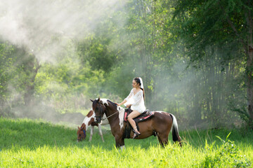 Young woman in white dress with horse. Woman riding red horse in the garden. Beautiful bride in a dress riding a horse.
