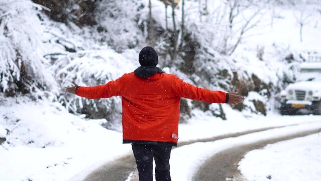 Rear view of an Indian man walking in the snow during snowfall with his arms raised at Manali in Himachal Pradesh, India. Tourist enjoying the snowfall during the winter. Nature Background. 