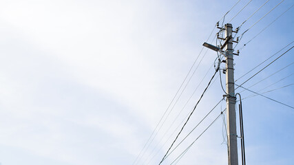Concrete pole of power lines in wires and with street lighting lamp against blue cloudy sky on...