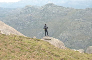 homem em cima de uma rocha numa encosta de montanha a observar as vistas montanhosas, viagem, turismo, caminhar, trilho de montanha