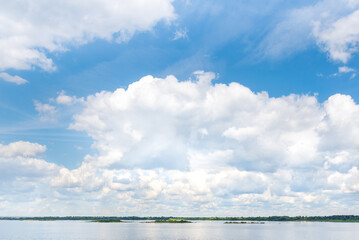 Cumulus clouds in the blue sky over the river in summer