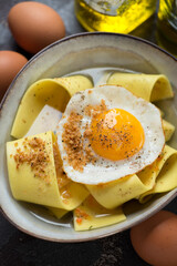 Bowl of rag pasta with crispy fried egg in parmesan broth, close-up, vertical shot, selective focus