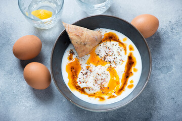 Bowl of turkish traditional cilbir on a light-blue stone background, horizontal shot, high angle view