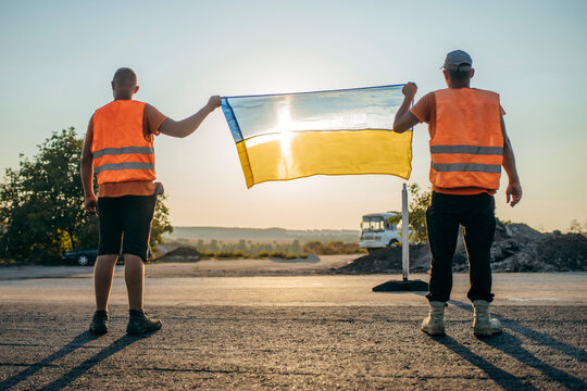 Two ukrainian young workers with Ukrainian flag in hands standing backwards