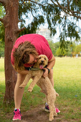 PASEO EN EL PARQUE. MUJER BESANDO A SU MASCOTA. FOTOGRAFIA VERTICAL. COLOR.
