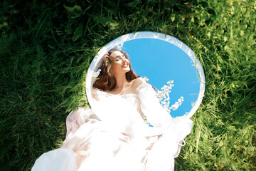 Young beautiful woman, reflection in the mirror. Spring photo in blooming garden.