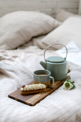Coffee in cup, beverage in teapot and eclair on cutting board