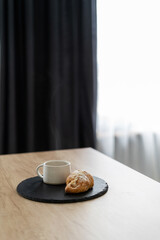 Mug of coffee with croissant on wooden table
