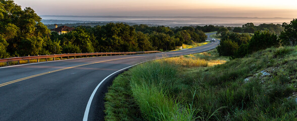 S shape curved road winding through a hilly terrain with a guard rail and a vehicle and hills in the distance, Guadalupe Valley, Texas