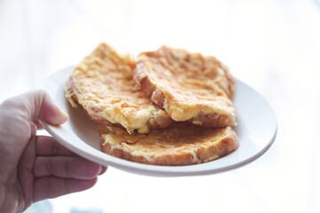 Close-up of a hand holding a plate of fried egg sandwiches in a white plate. The concept of a quick breakfast