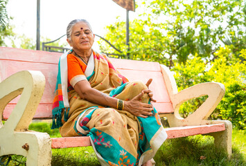 Senior woman suffering from kee joint pain after walking while sitting at park - concept of arthritis, unhealthy and illness - obrazy, fototapety, plakaty