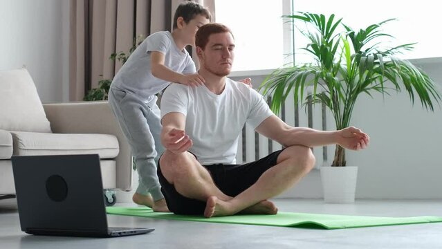 dad doing morning exercises while active energetic child son playing. father working and doing yoga exercise at home for stress relief relaxing with naughty little kid. little boy hugs dad from behind