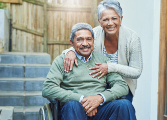 Shes means the world to me. Portrait of a cheerful elderly man seated in a wheelchair while being held by his loving wife outside at home during the day.