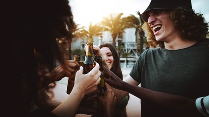 Happy friends cheering beer bottles on summer sunset background - Young people celebrating party...