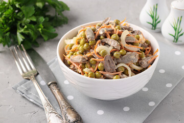 Salad with chicken hearts, canned peas, onions and carrots in a white bowl on a gray background