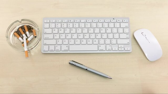 Office desk with keyboard, mouse, pen, ashtray with extinguished cigarettes. Bad habits, nervous work, long working hours. Stop motion animation.