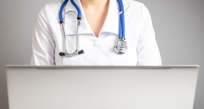 Online medical consultation concept. Doctor with stethoscope treating patient using laptop and Internet. Woman in lab coat sitting at table with computer. Telemedicine, telehealth concept. photo