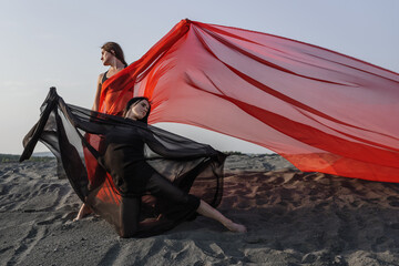 Two girls in black and red flowing fabric pose on sand dune