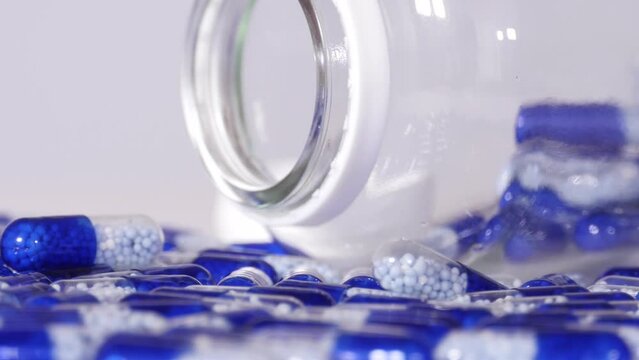 Blue white medical medicine capsules and transparent jar packaging rotate seamlessly, macro shot.