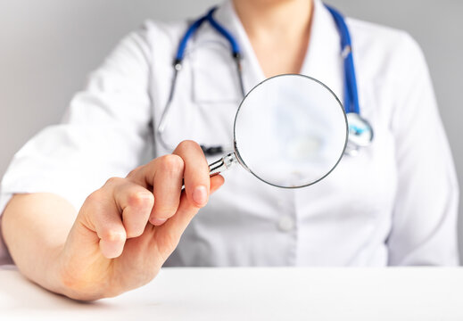 Medical checkup concept. Doctor holding magnifying glass. Woman in lab coat sitting at table with loupe. Health care and regular physical examination. High quality photo