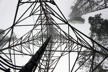 Abstract view in silhouette looking up from directly underneath a telecommunication mast tailing off into the mist. Microwave link and TV transmitter towers. No people.