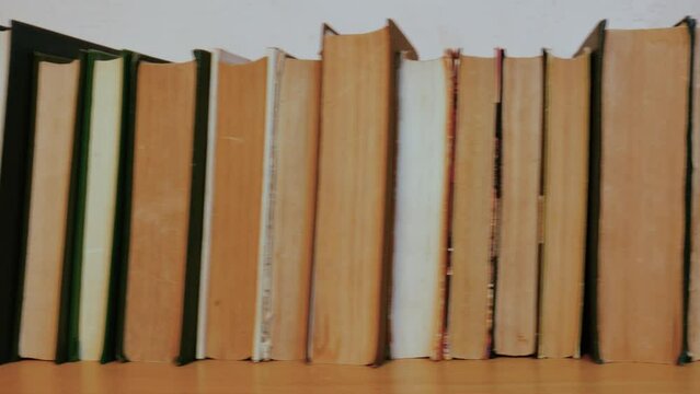 Dolly shot of a row of old vintage books with yellowed faded pages and covers on a table or bookshelf in a library