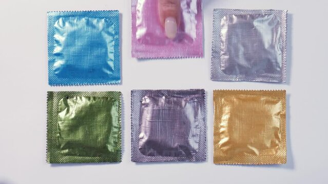 A woman's finger picks up a pink condom among the multi-colored packages, then takes another one. Sexual relations, safer sex planning, contraception, STD prevention.