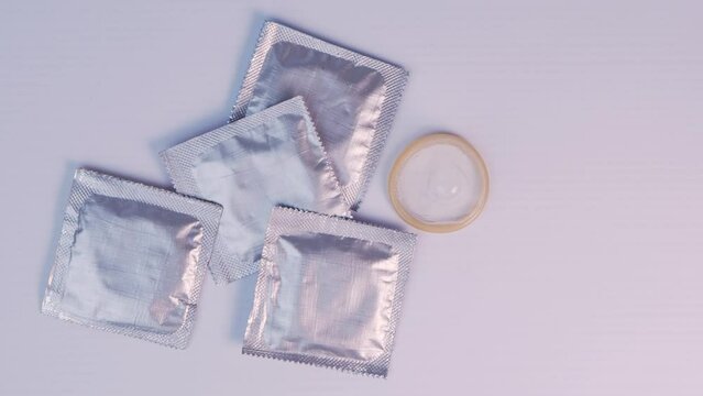 Woman's finger picks up a condom among several silver packages and puts AIDS awareness red ribbon.