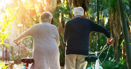 Where shall we go dear. Rearview shot of a elderly couple pushing their bicycles together outside in a park.