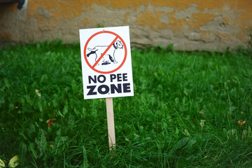 No pee zone square dog sign on wooden stick on green grass lawn