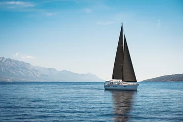 Fototapeten White yacht with black sails in the sea against a background of blue sky and mountains © Maxim Sokolov