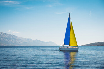 A white yacht with sails the color of the Ukrainian flag in the sea against a background of blue...