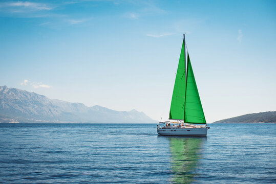 White yacht with green sails in the sea against a background of blue sky and mountains