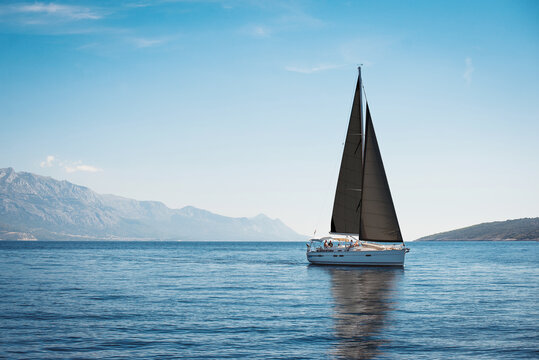 White yacht with black sails in the sea against a background of blue sky and mountains