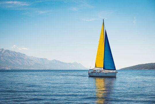 A white yacht with Swedish flag sails at sea against a background of blue sky and mountains