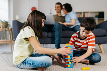 Obraz premium Kids playing together on the floor while parents using a laptop in the living room at home. Childhood and family concept.