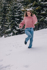 A young, slender, long-haired girl runs through the snow in a winter forest in the mountains.