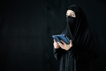 mysterious muslim woman using tablet computer on black background