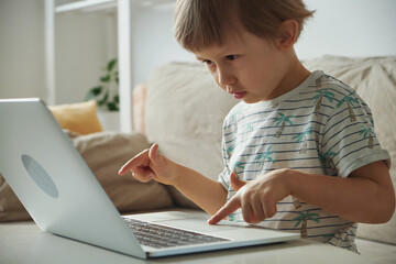 Fototapeta na wymiar Happy child typing using laptop sitting on sofa at home, Homeschooling, remote education