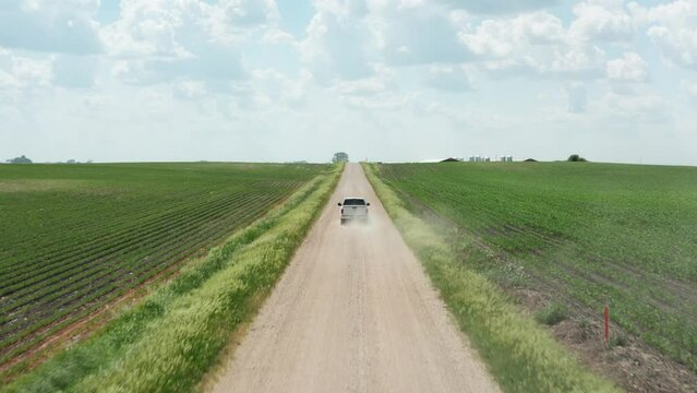 Aerial, pickup truck driving on unpaved rural farmland countryside dirt road on summer day. 