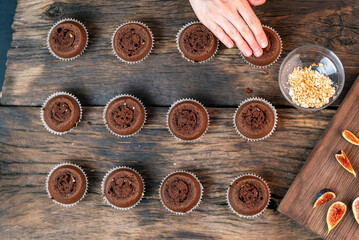 Lots of little coffee cupcakes on wooden table. Cook decorates chocolate muffins with fig pieces. Top view
