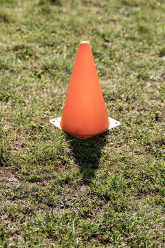 Orange cap on green grass. Sports equipment to mark border. Pyramid figure. Cone on lawn. 