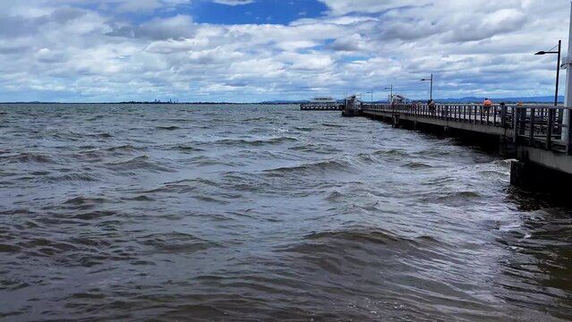 Slow panning shot of ocean waves and boardwalk at Woody Point Jetty on a cold sunny morning